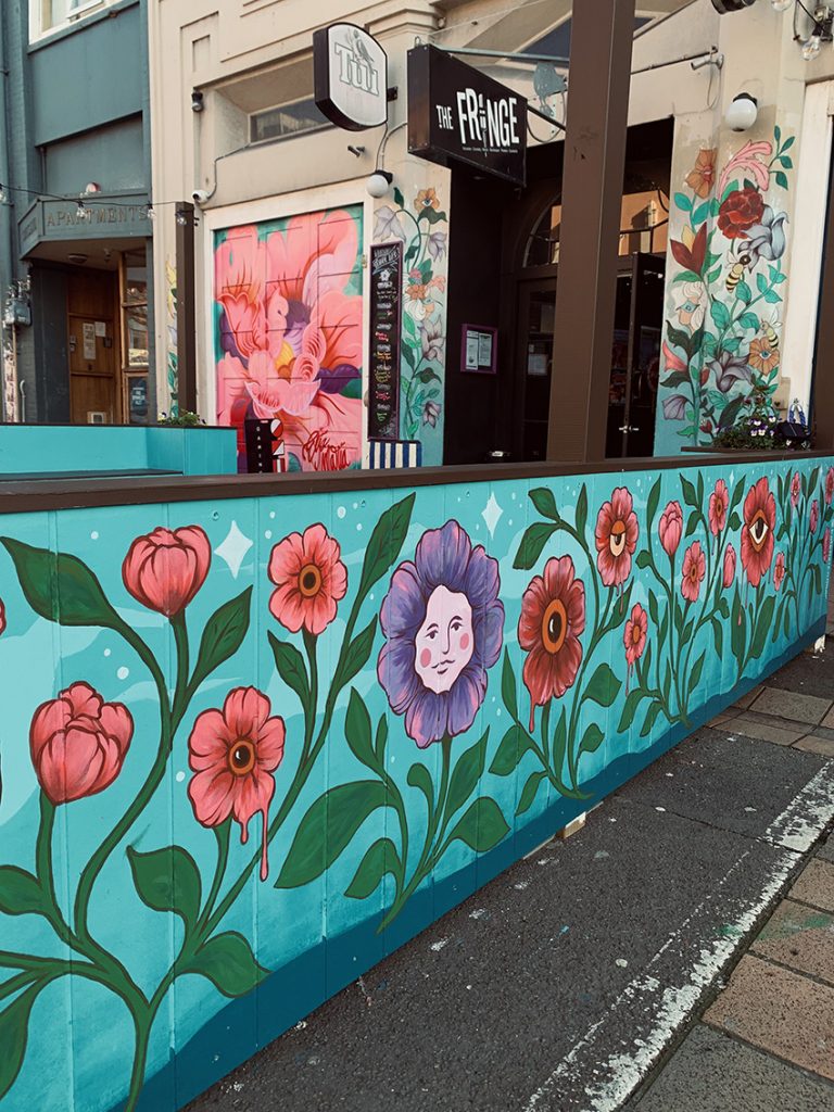 Fringe Bar exterior mural featuring large pink and red flowers on a blue background, hand-painted by Kate Helen Muir.