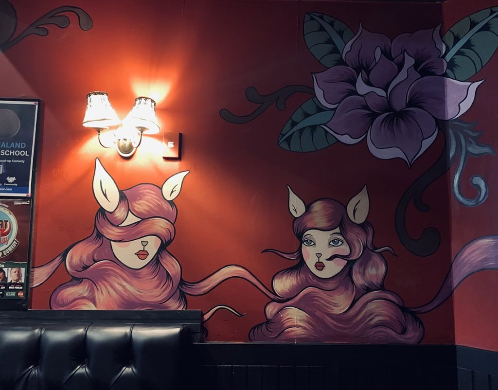 Two illustrated women with long flowing hair, fox-like ears, and stylised features painted on a red wall at the Fringe Bar in Wellington